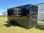 A black food truck trailer parked on grass outdoors, with a serving window extended on the side. The trailer has a glossy reflective black finish, diamond plate side panels, dual wheels, and a hitch at the back.